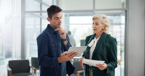 Man and older woman reviewing a tablet and papers in an office