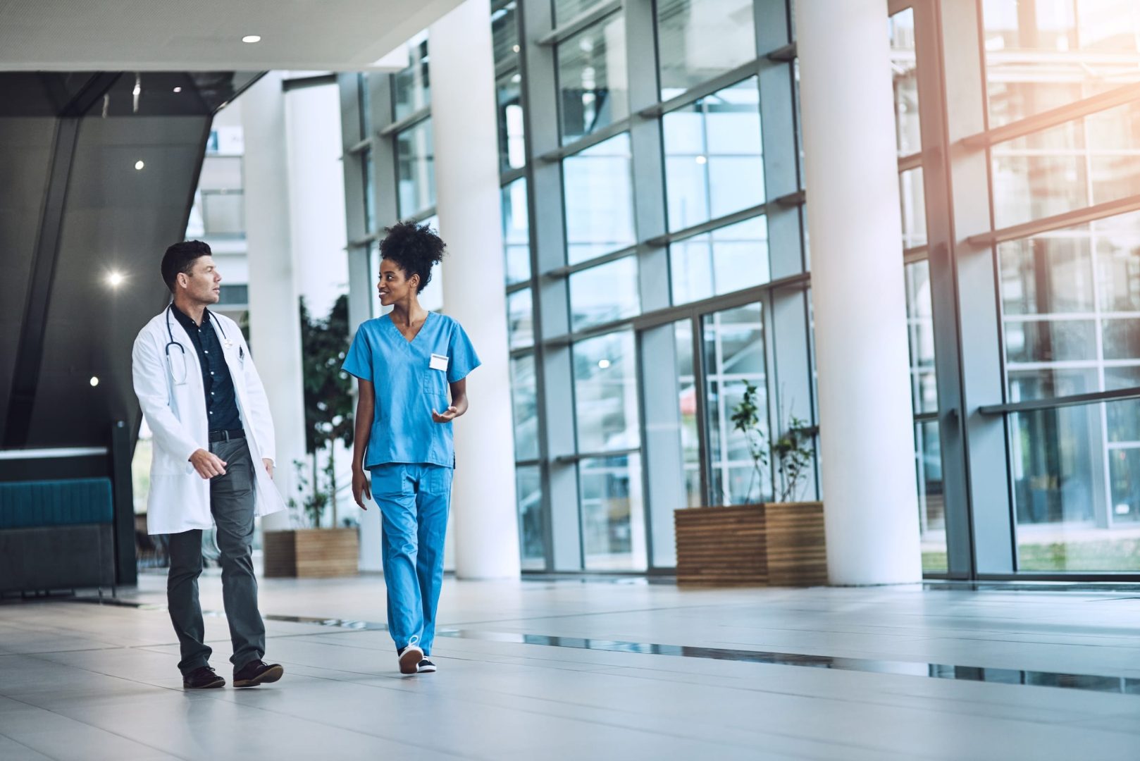 Doctor in a white coat and a nurse in scrubs walking through a hospital corridor